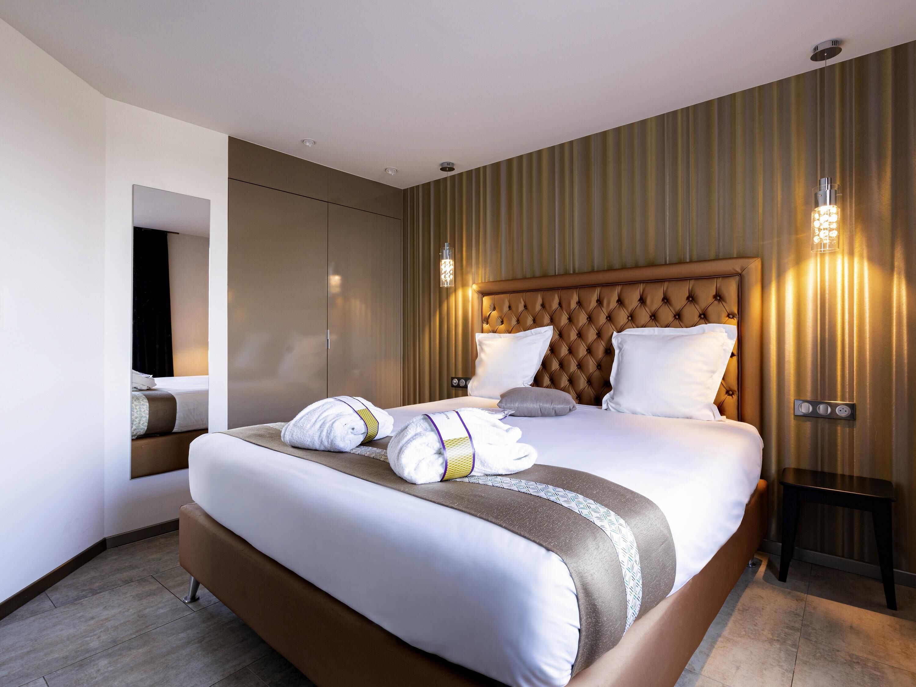 A modern hotel room with a large bed, a built-in TV, and a bedside table with a lamp.
