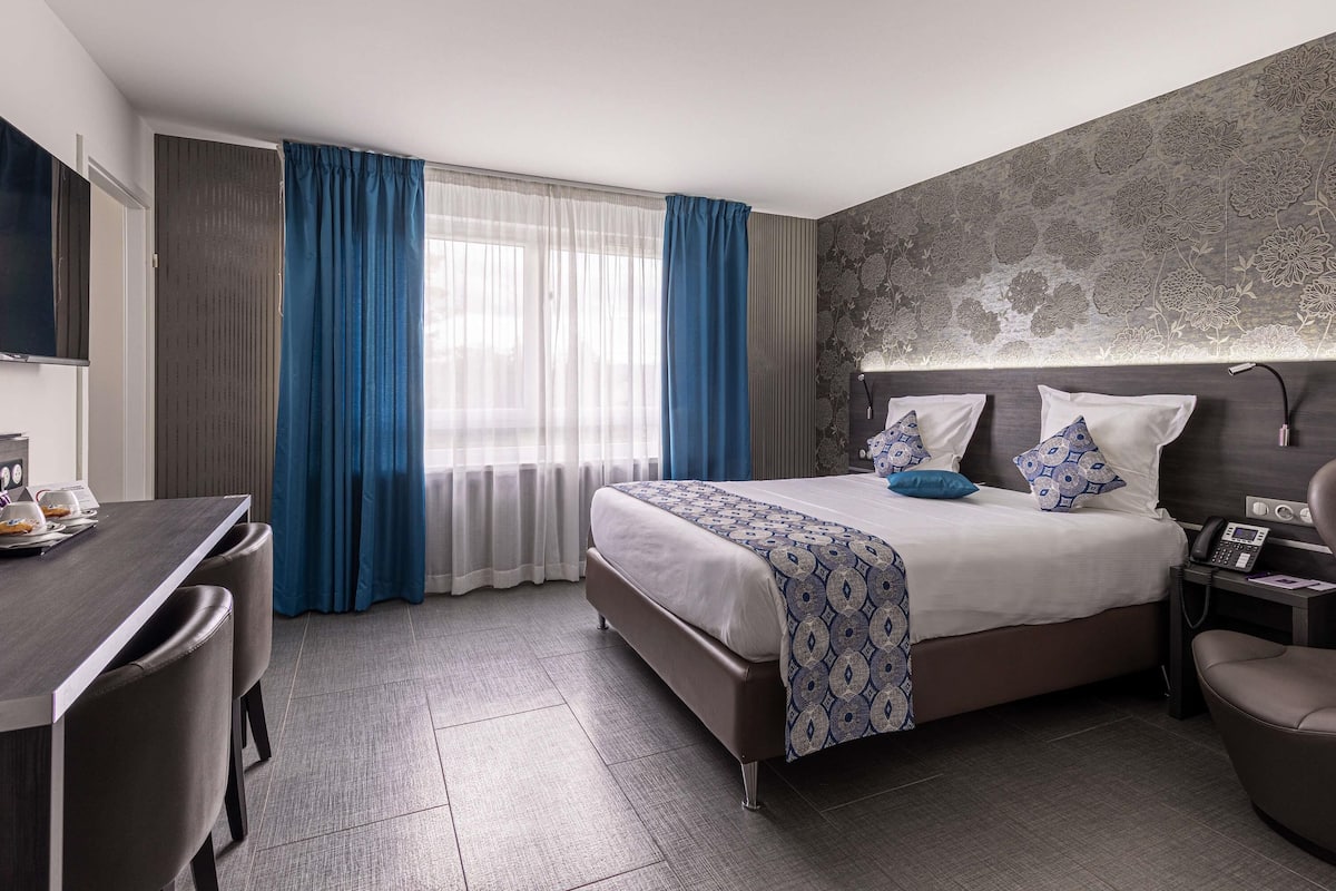 A hotel room with a bed, bedside table, desk, and chair.