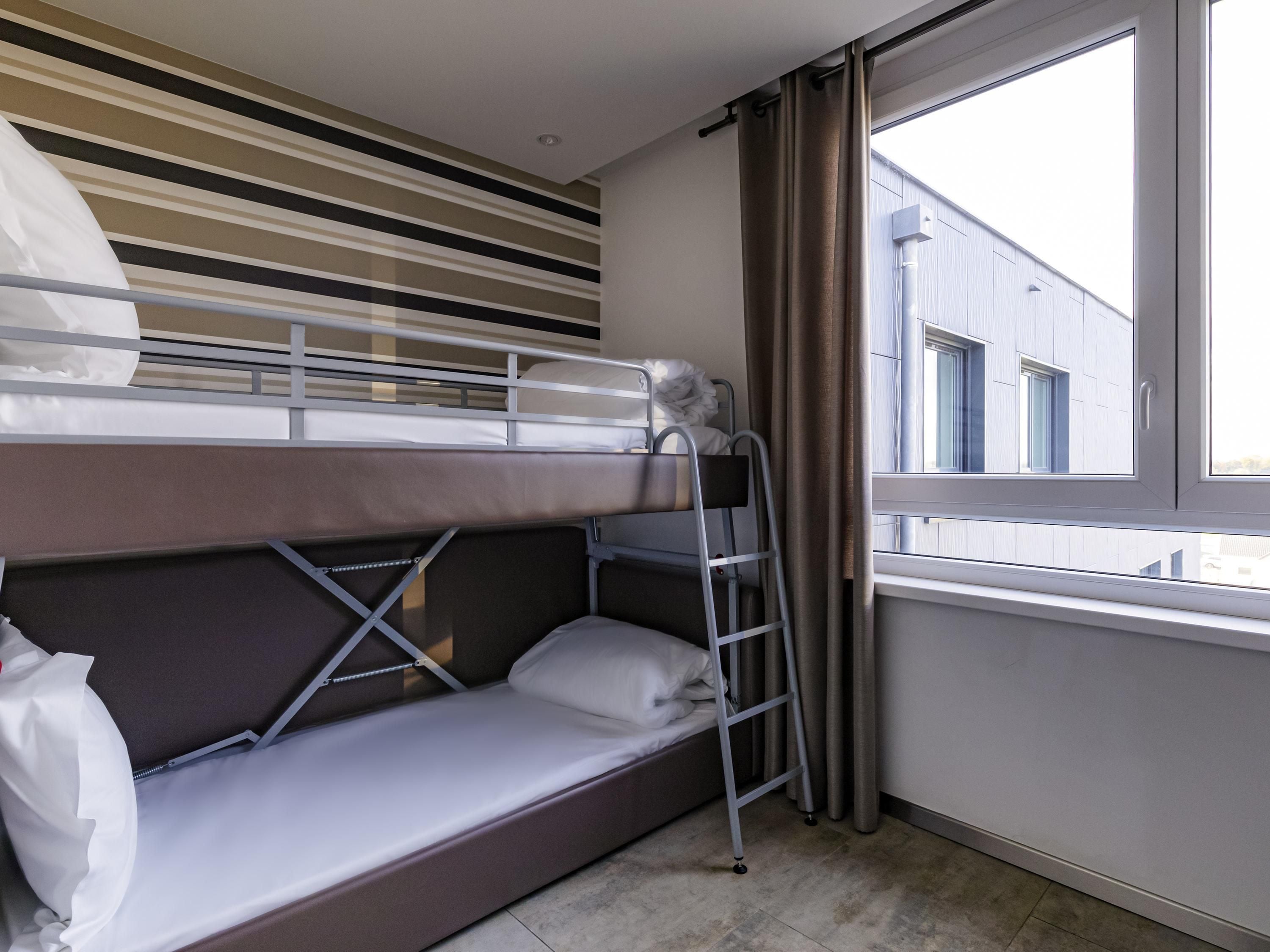 A bunk bed room with a window, curtains, and a striped wall.