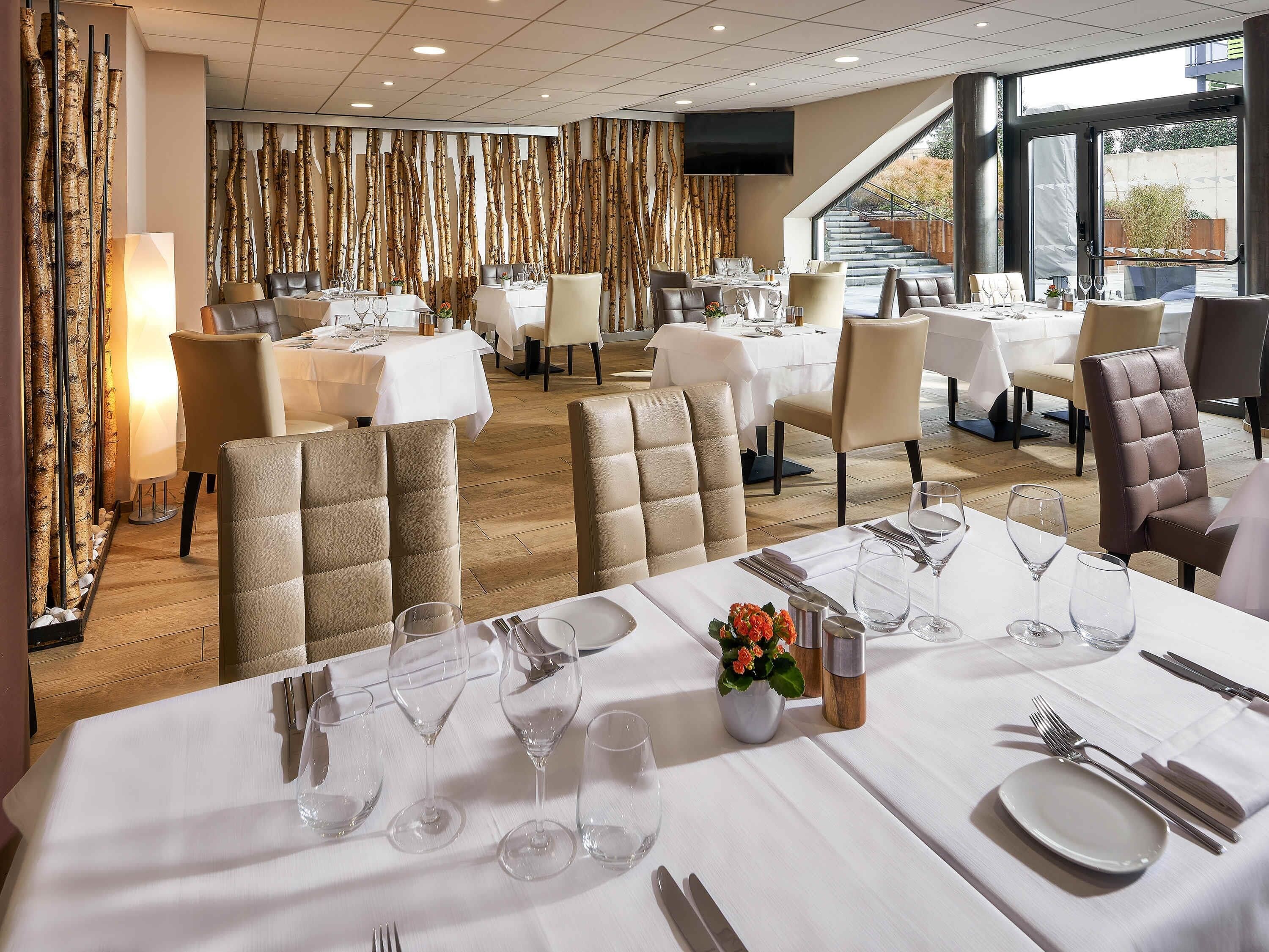 A restaurant with multiple tables set for dining, a large TV screen, and a view of the outdoors.