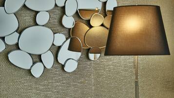 A room with a patterned carpet, a lamp with a brown shade, and various mirrors of different shapes and sizes.