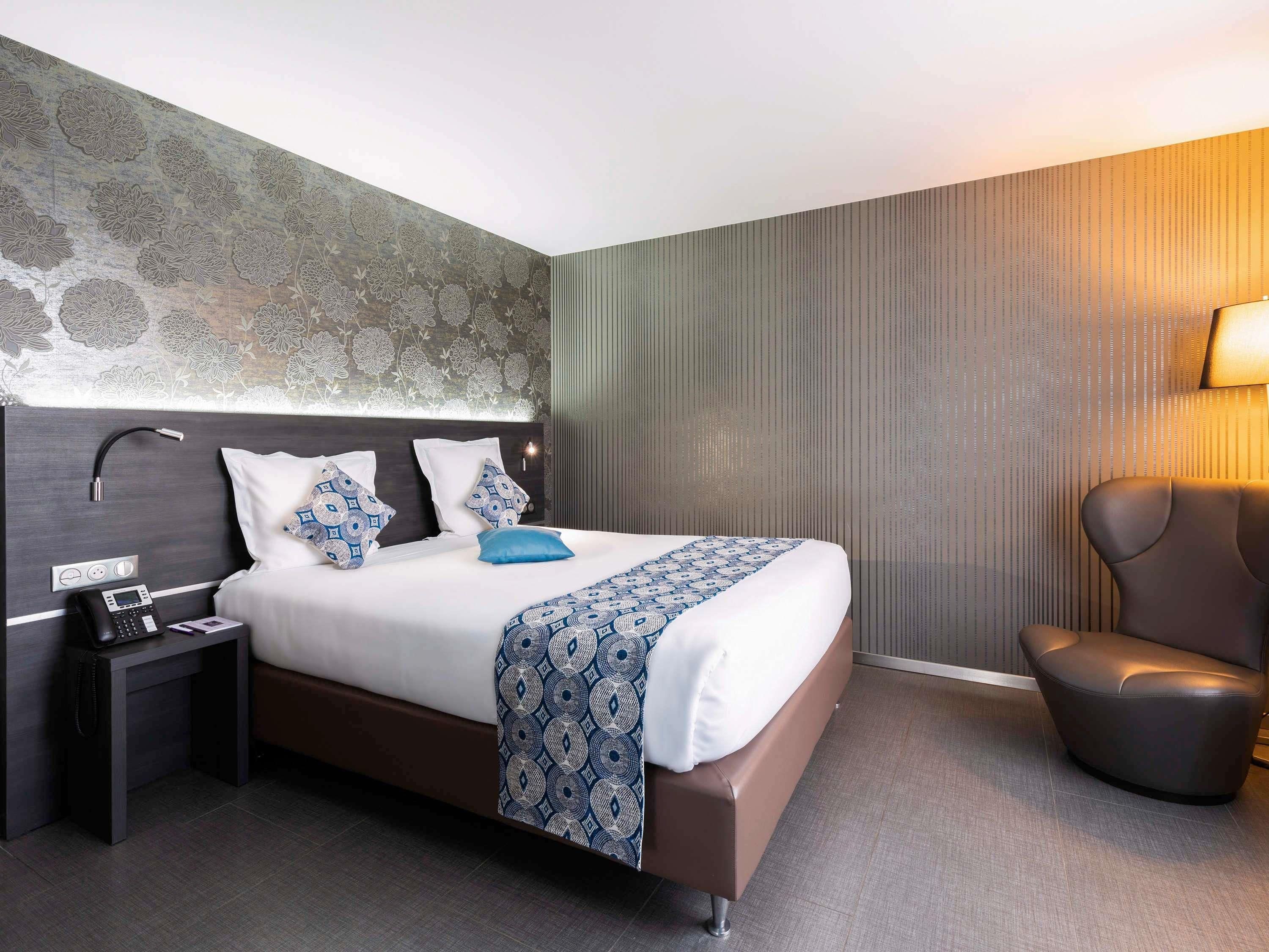 Ein modernes Hotelzimmer mit einem großen Bett, einem Nachttischtelefon, einem Beistelltisch und einem Sessel.