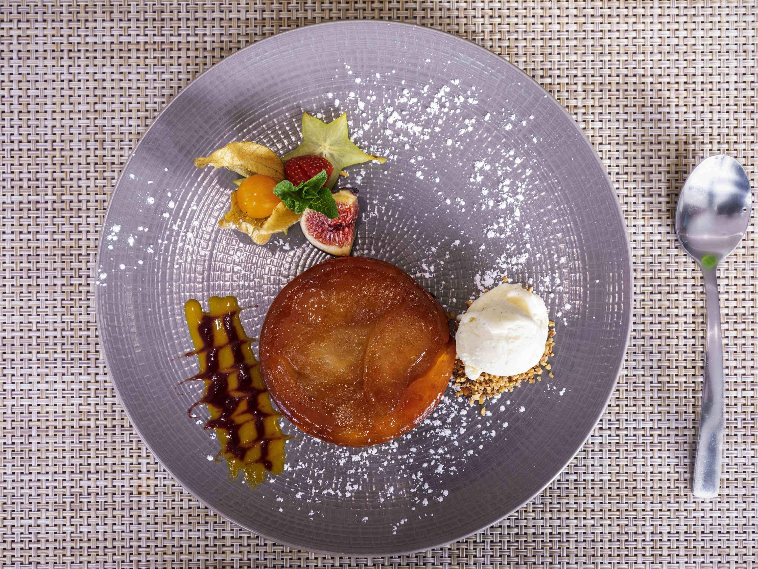 Un plato de postre con una manzana caramelizada, una bola de helado y una guarnición de frutas.