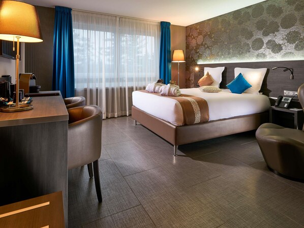 A hotel room with a bed, desk, chairs, and a nightstand with a phone.