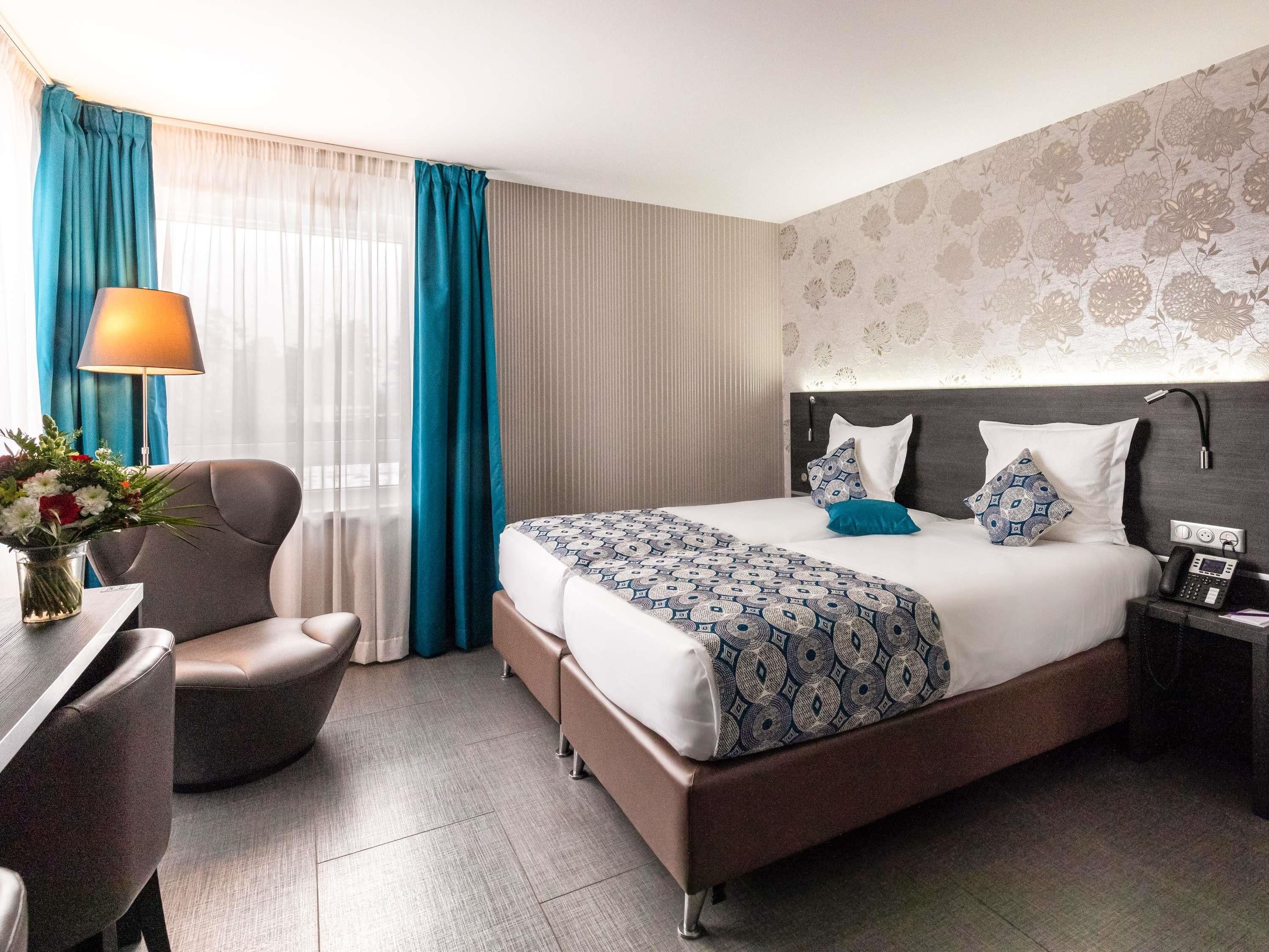 Una habitación de hotel con cama, escritorio, silla, lámpara y mesita de noche con teléfono.