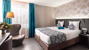 Una habitación de hotel con cama, escritorio, silla, lámpara y mesita de noche con teléfono.