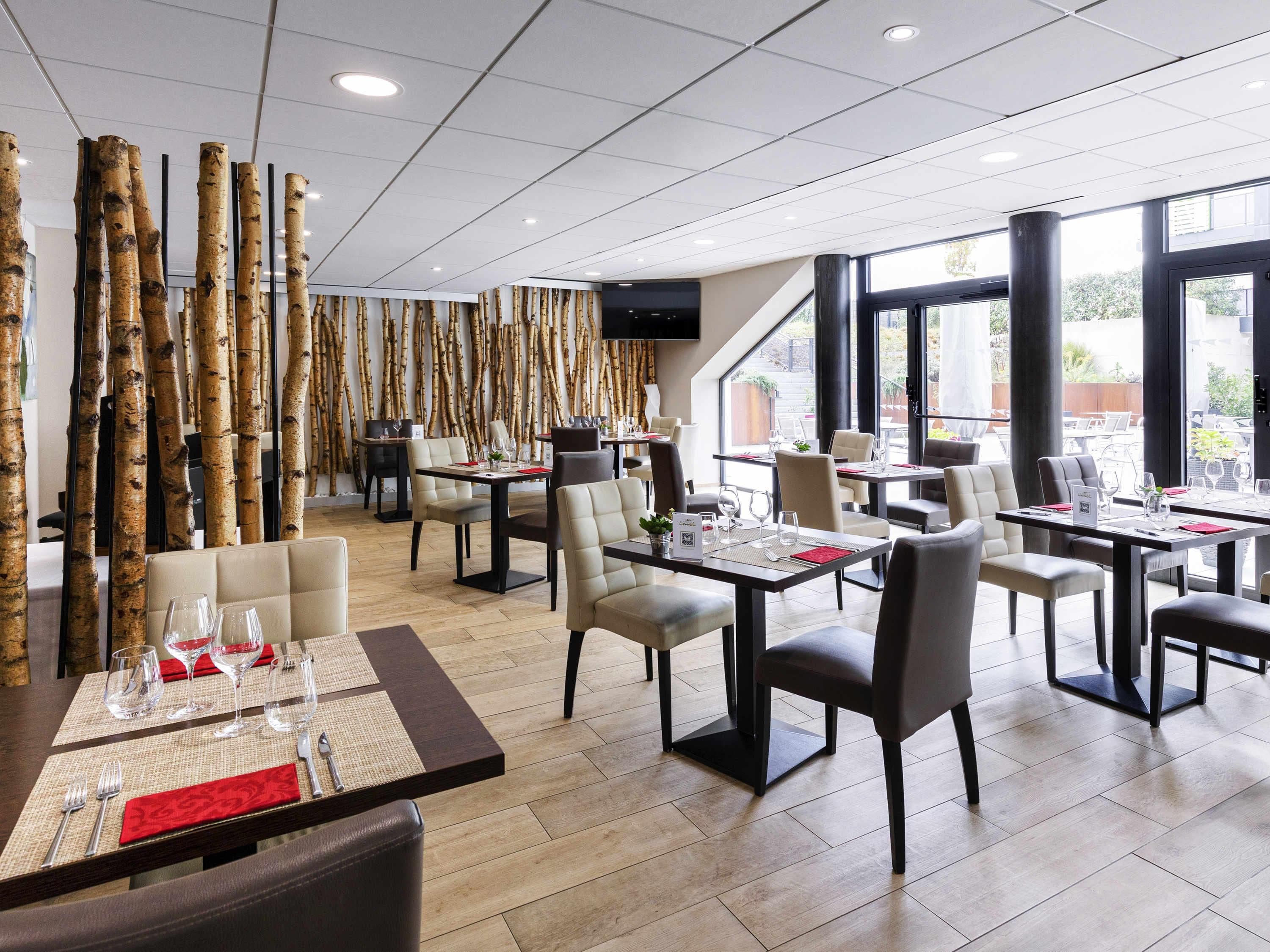 A modern restaurant with high tables and chairs, a wooden wall feature, and large windows offering a view.