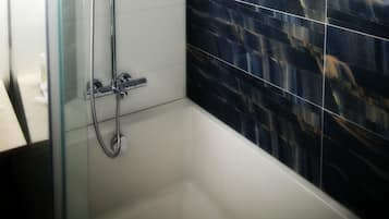 A shower area with a glass door, a handheld showerhead, and a wall with a dark, patterned tile design.