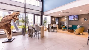 A modern hotel lobby with large windows, a reception desk, seating area, and a mounted TV.