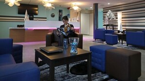Un vestíbulo moderno con asientos azules, un mostrador de recepción y un jarrón grande sobre una mesa.