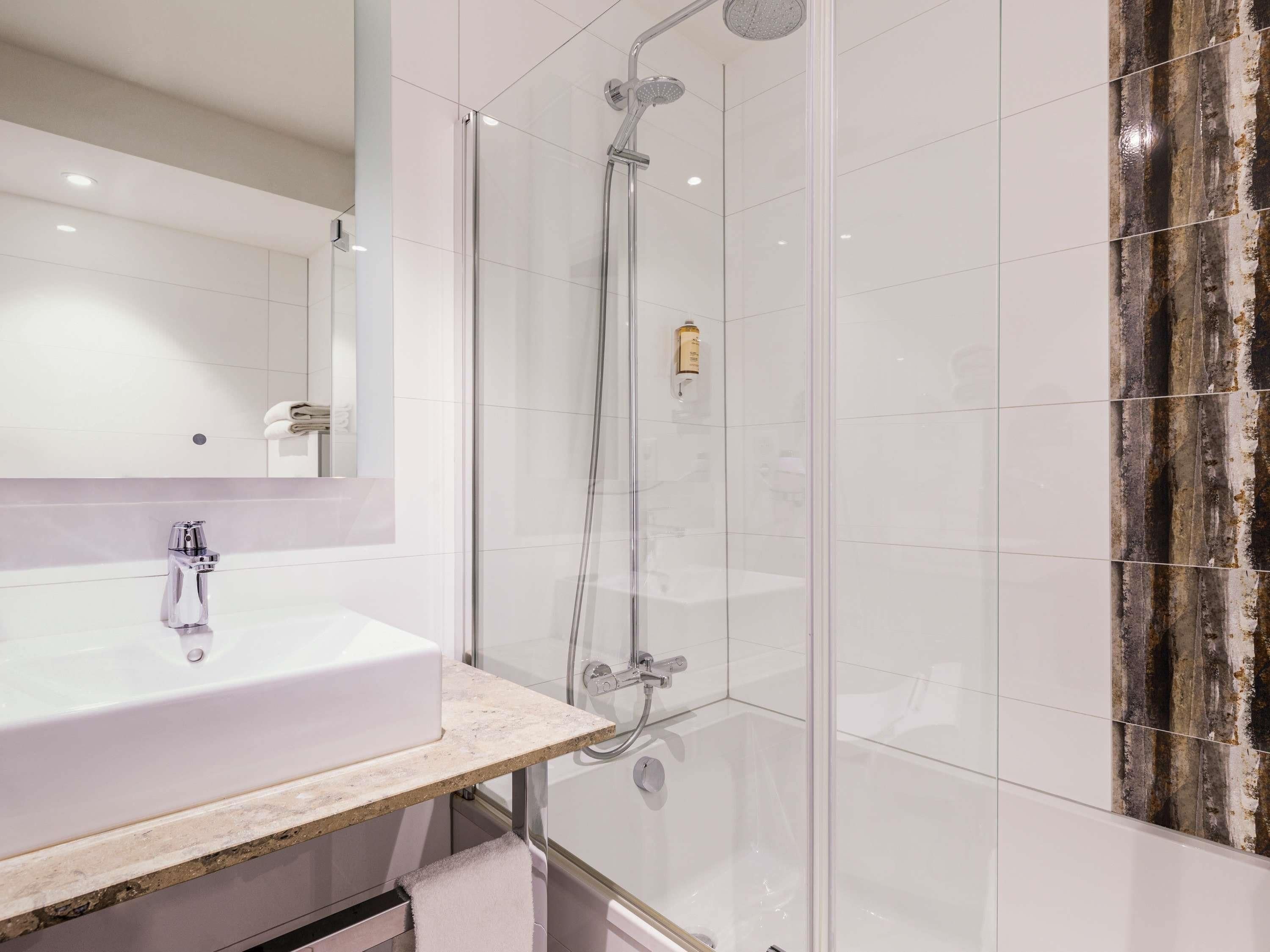 Ein modernes Badezimmer mit einer gläsernen Duschkabine, einem weißen Waschbecken und einer Marmorplatte.