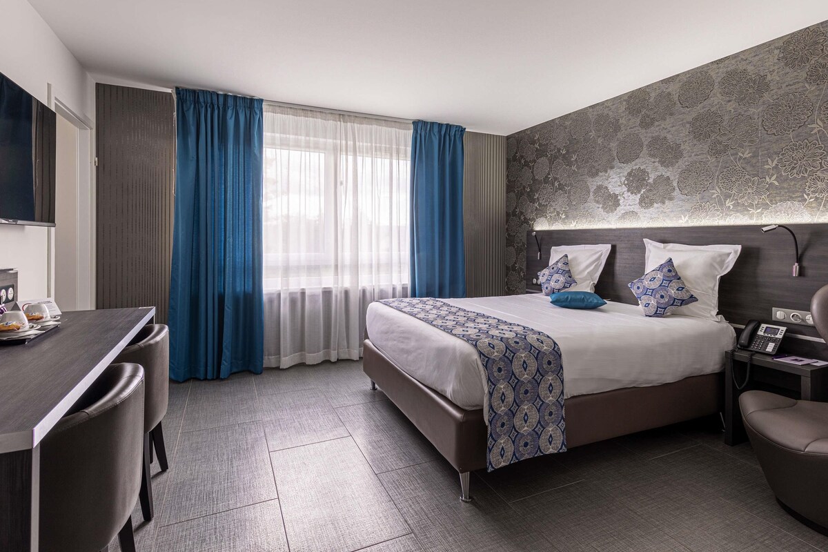 A hotel room with a bed, bedside table, desk, and chair.