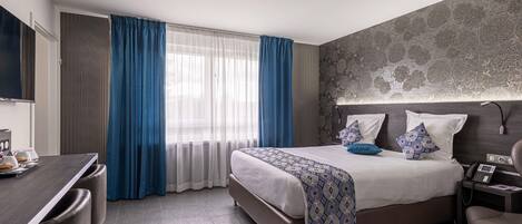 A hotel room with a bed, bedside table, desk, and chair.