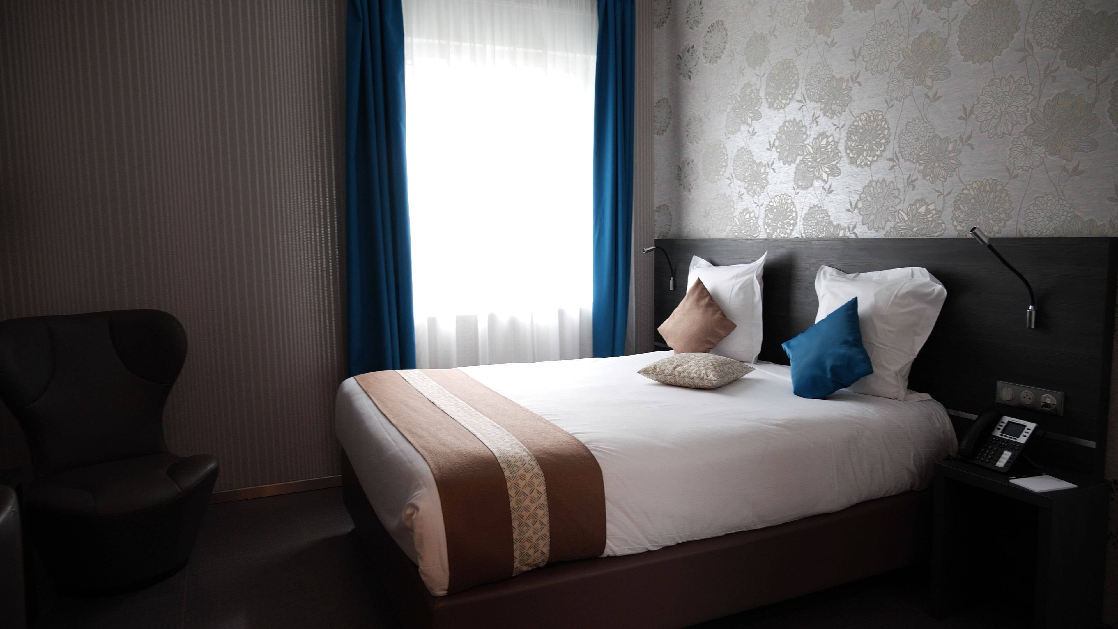 A hotel room with a large bed, a bedside table with a phone, and a chair.