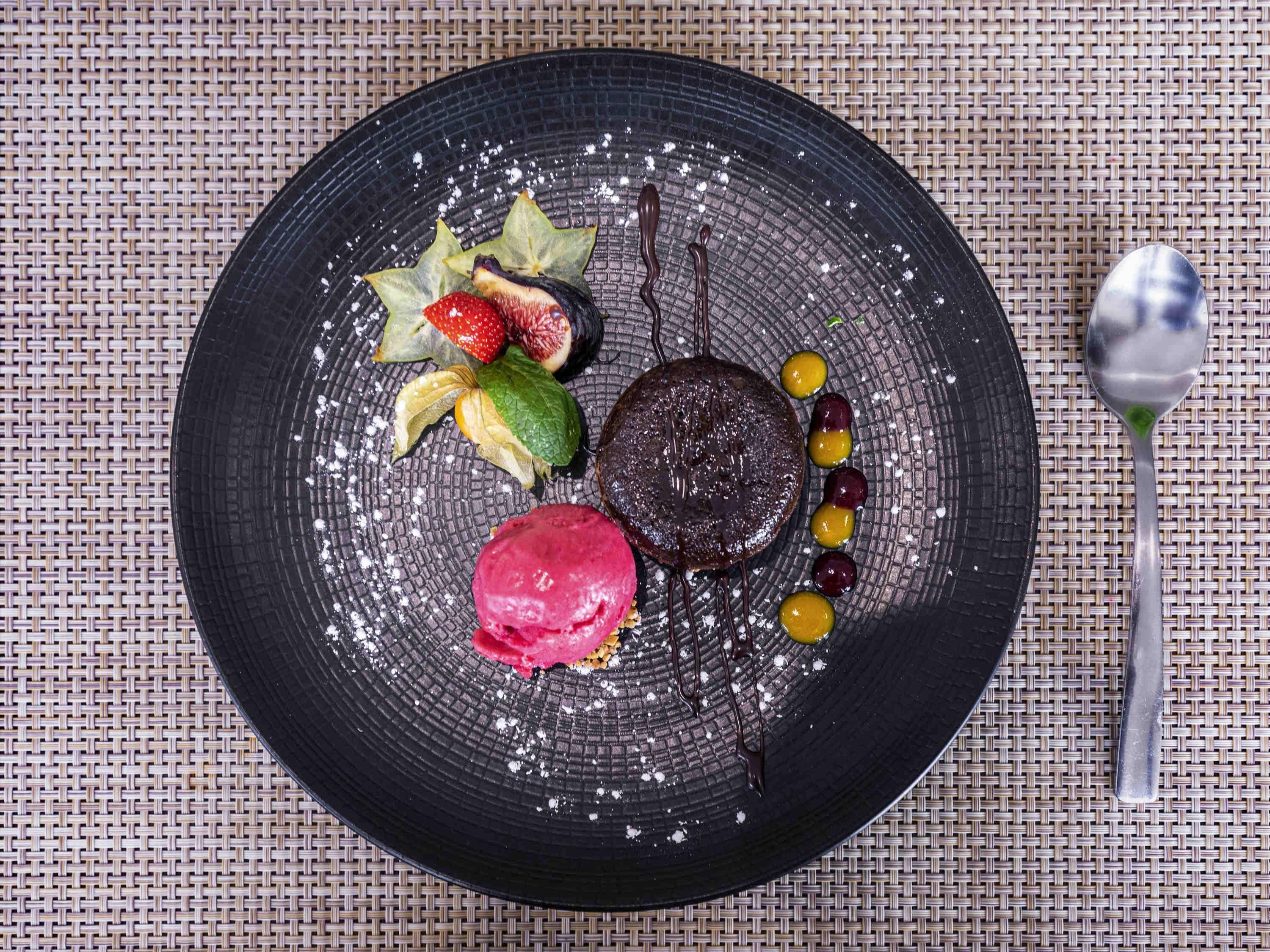 Plat de postres amb diversos elements, com ara un pastís de xocolata, freses, figues i una bola de gelat.