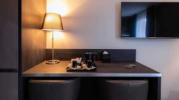 A hotel room with a desk, two chairs, a television mounted on the wall, and a lamp on the desk.