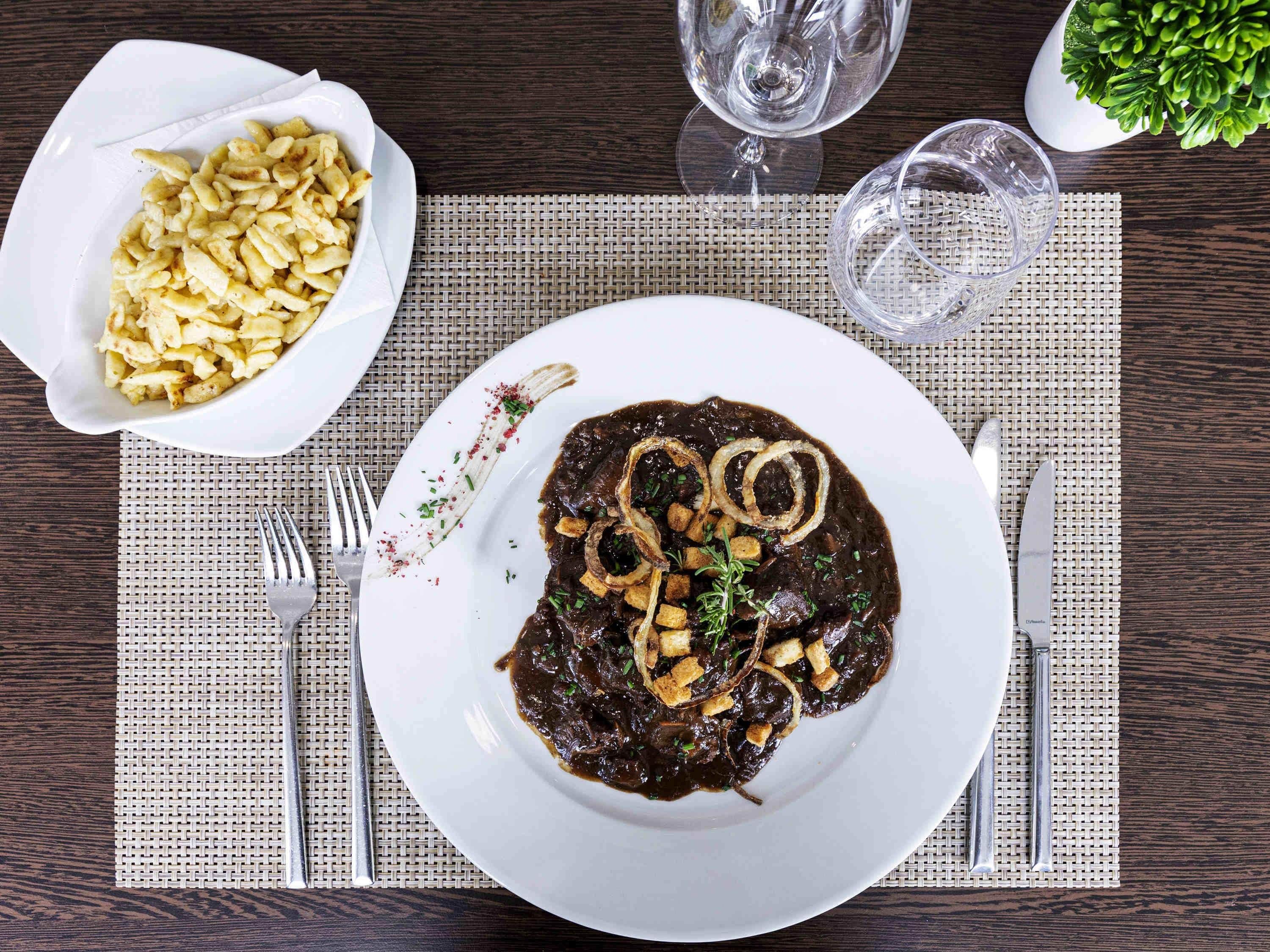 En tallrik med mat, bestående av en mörk sås, lök och örter, en skål med pasta och ett glas vatten på ett bord.