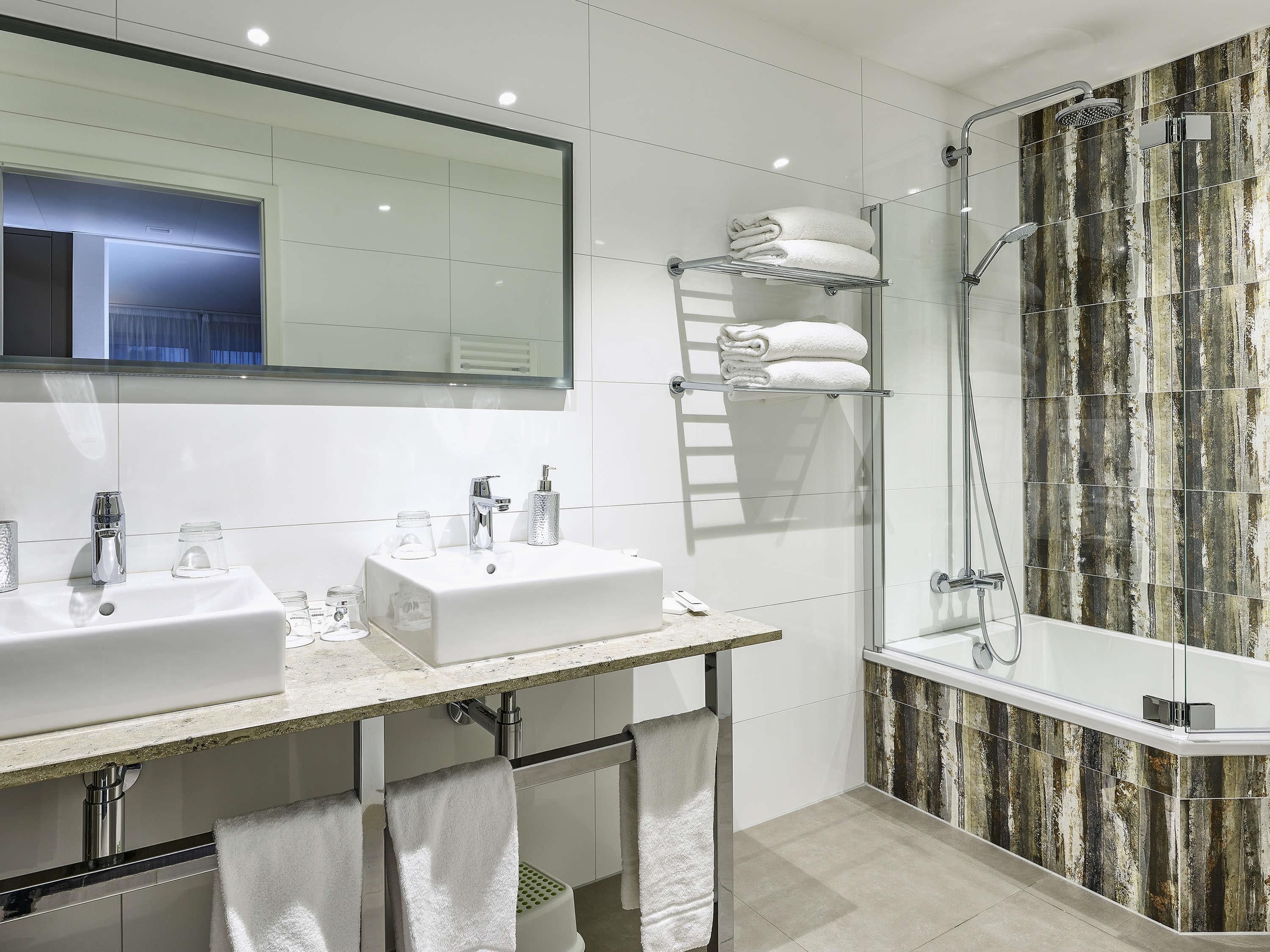 Une salle de bain moderne avec deux lavabos, un grand miroir, une douche en verre et un porte-serviettes.