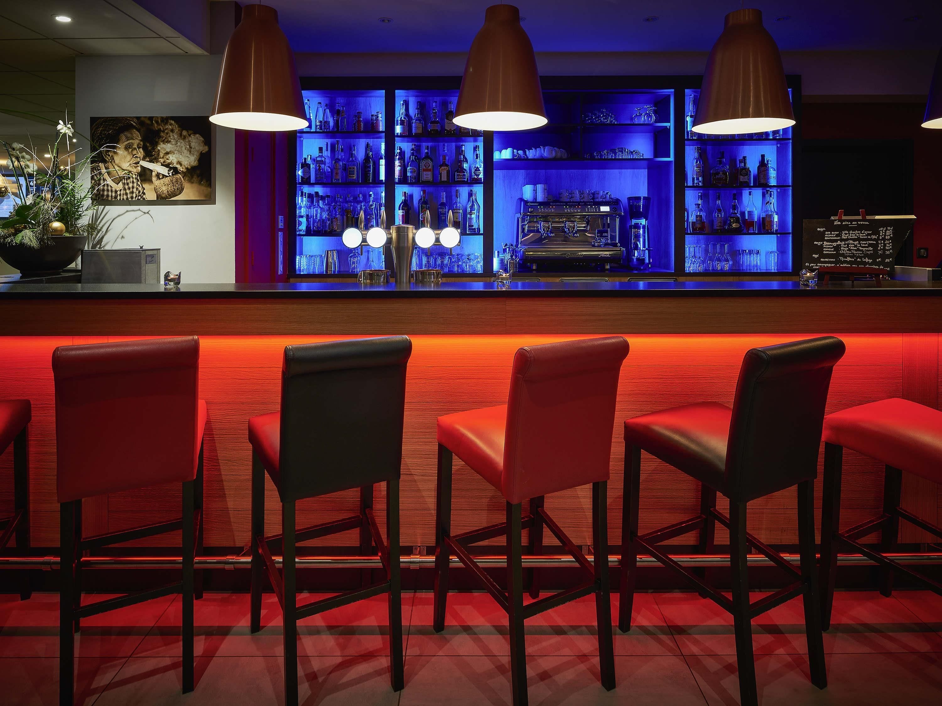 A bar area with red chairs, a bar counter, and shelves of bottles.