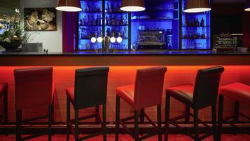 Zona de bar con sillas rojas, barra y estanterías llenas de botellas.