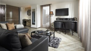 A modern living room with a sofa, coffee table, and a dining area with chairs and a TV. - Mercure Bale Mulhouse Aeroport (Blotzheim)