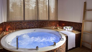 A hot tub with a tiled surround, a towel rack, and a small table with a glass of water and a candle.