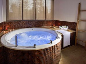 Un bain à remous entouré de carreaux, un porte-serviettes et une petite table avec un verre d’eau et une bougie.