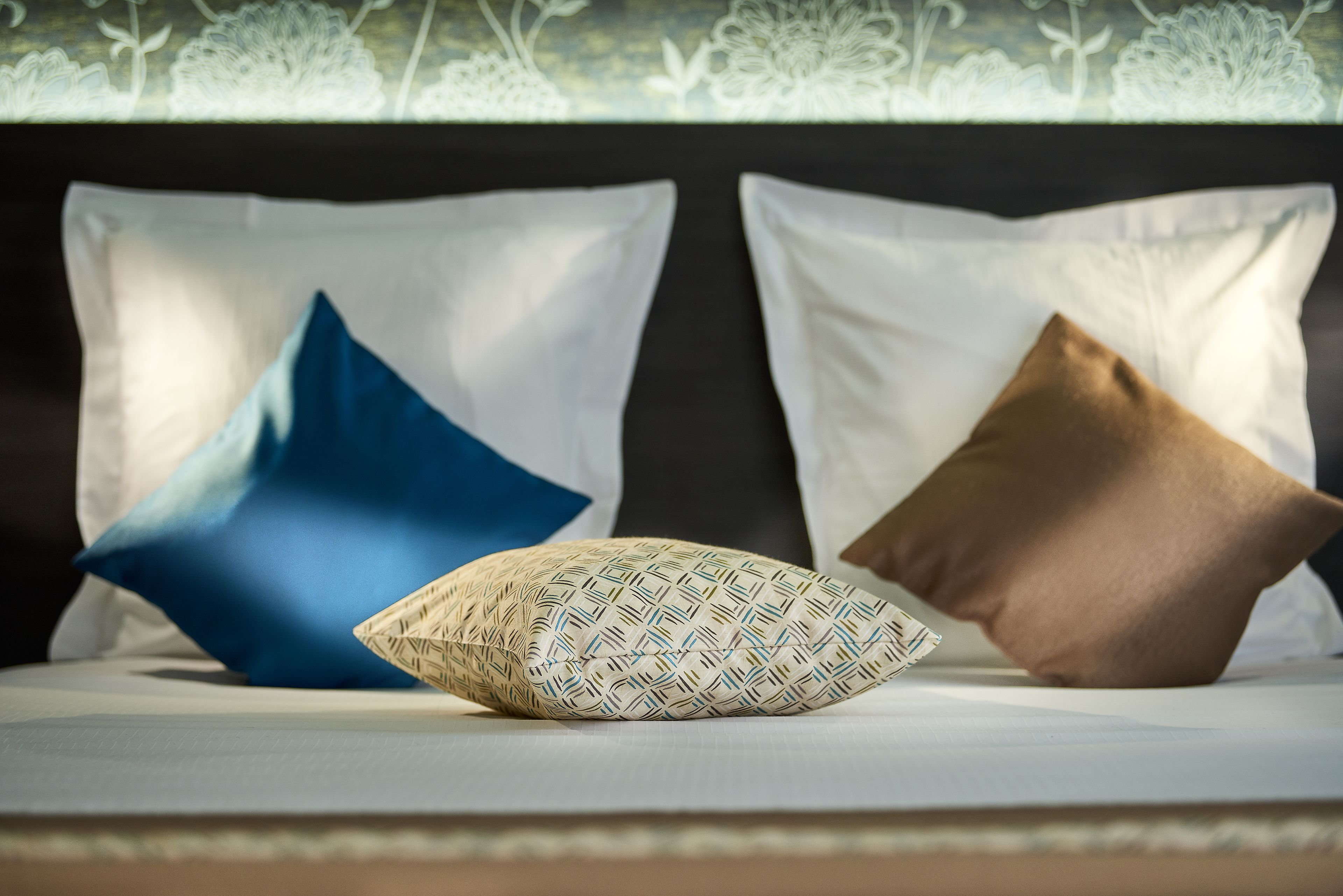 Ein Bett mit drei Kissen in verschiedenen Mustern und Farben.