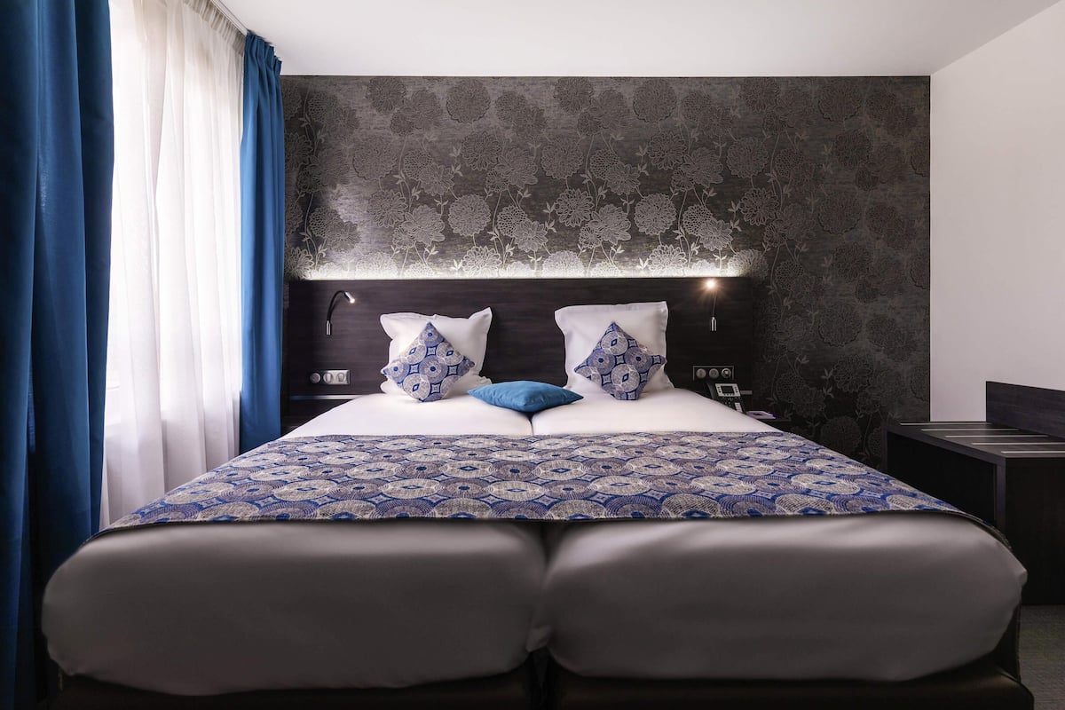 A modern bedroom with a large bed, a bedside table, a nightstand, and a wall-mounted lamp.