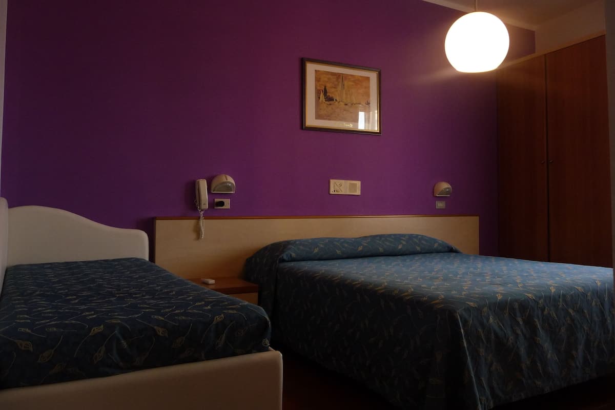 A room with two beds, purple walls, a framed picture, a bedside lamp, and a phone.