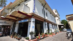 Un hotel llamado "Hotel Azzurra" con un letrero, plantas en macetas y una calle adoquinada.