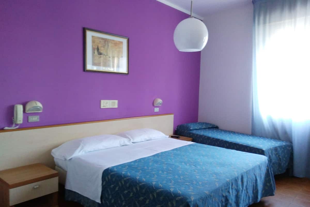 A room with two beds, a wooden nightstand, a wall-mounted telephone, and a ceiling light fixture.