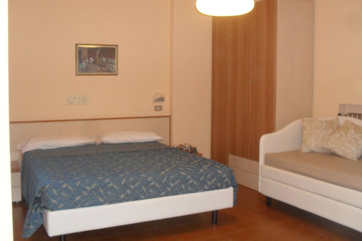 A bedroom with a bed, a sofa, a painting on the wall, and a light fixture.