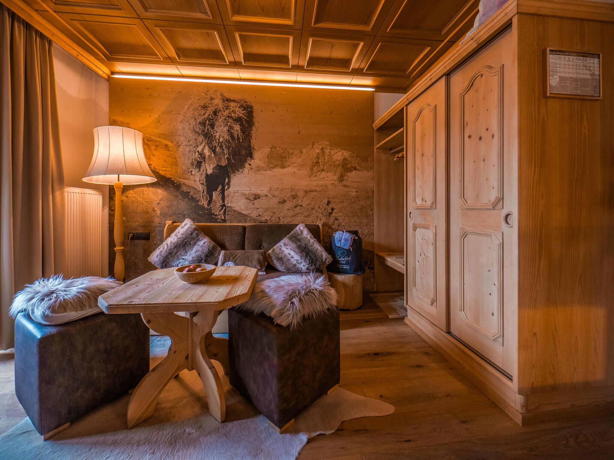 Um quarto aconchegante com teto de madeira, um sofá com almofadas de pele, uma mesa com uma tigela e uma luminária.