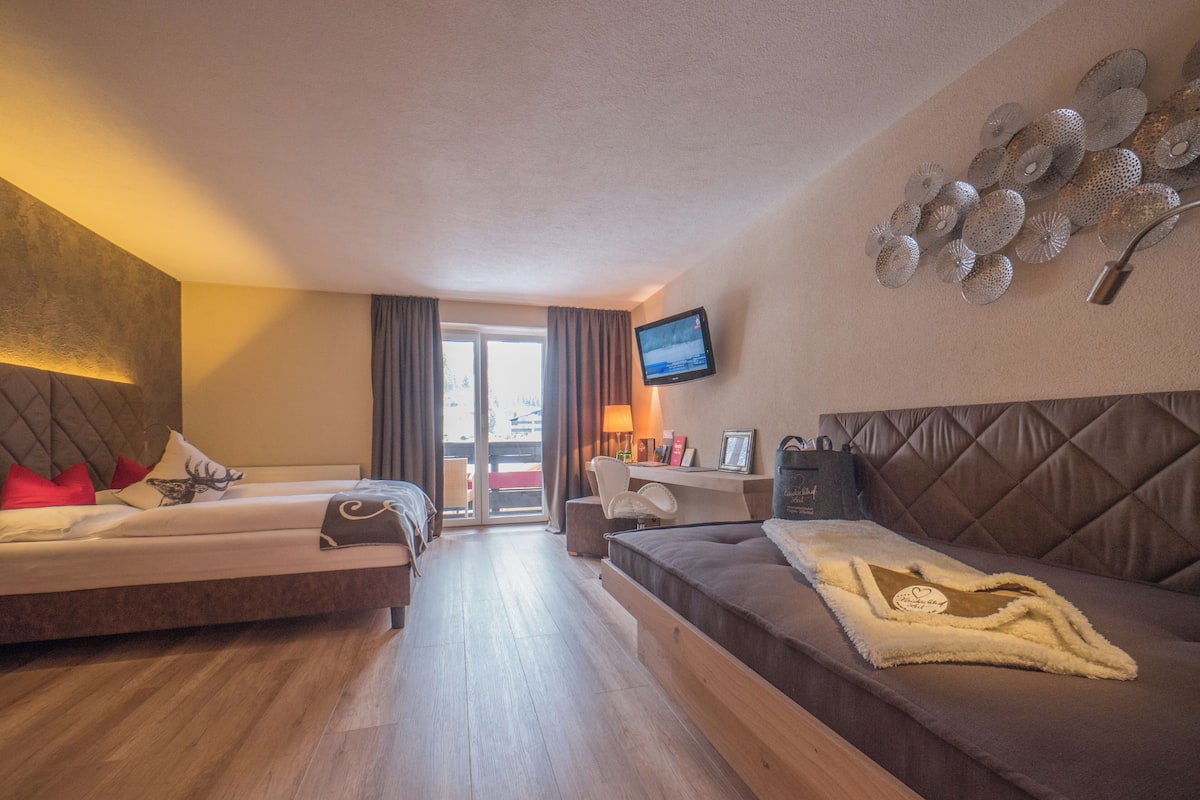 Ein Hotelzimmer mit zwei Betten, einem Sofa, einem Fernseher und einem Balkon mit Blick.