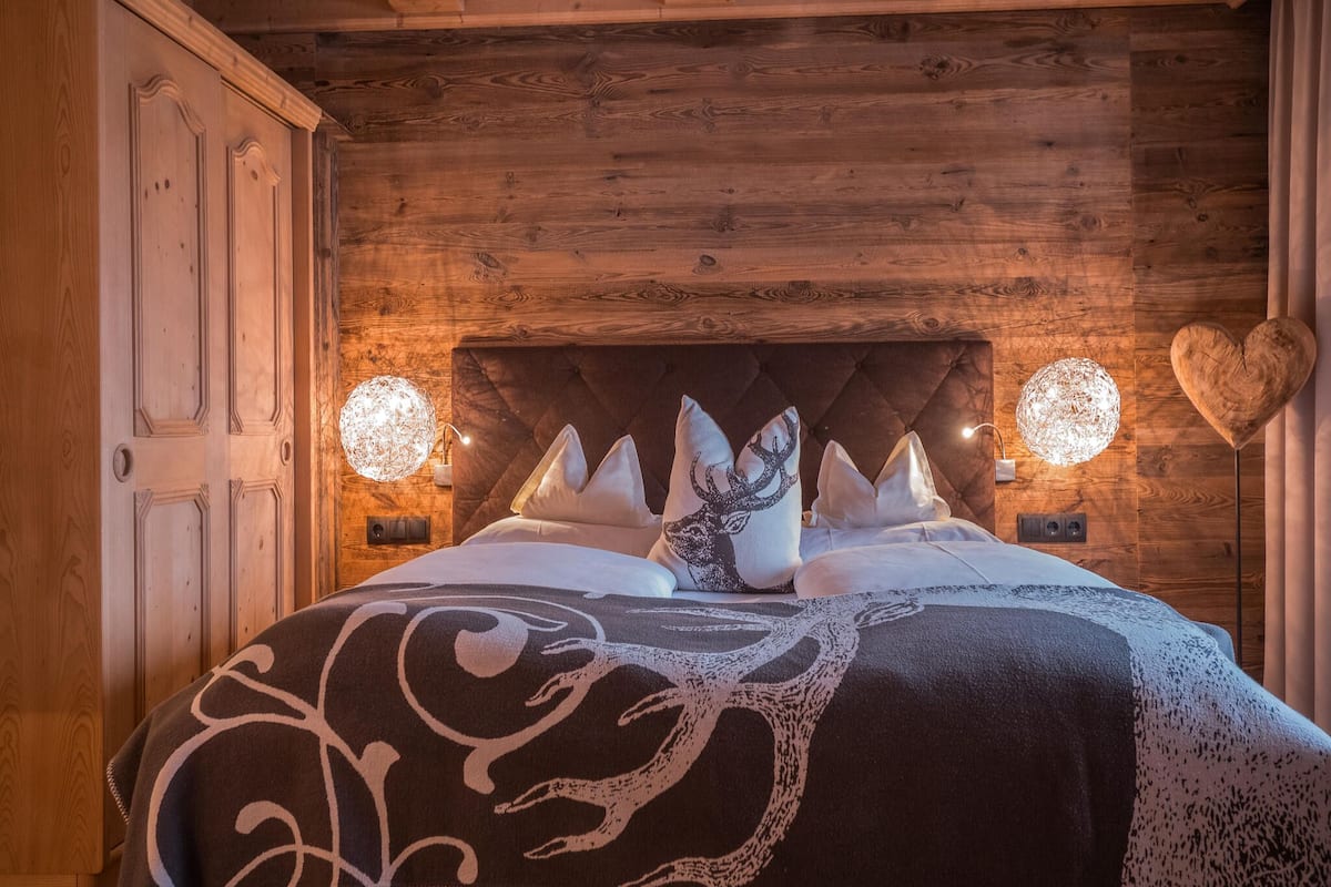 Ein Schlafzimmer mit Holzwandverkleidung, einem gepolsterten Kopfteil, einem Bett mit dekorativen Kissen und zwei wandmontierten, kugelförmigen Leuchten.