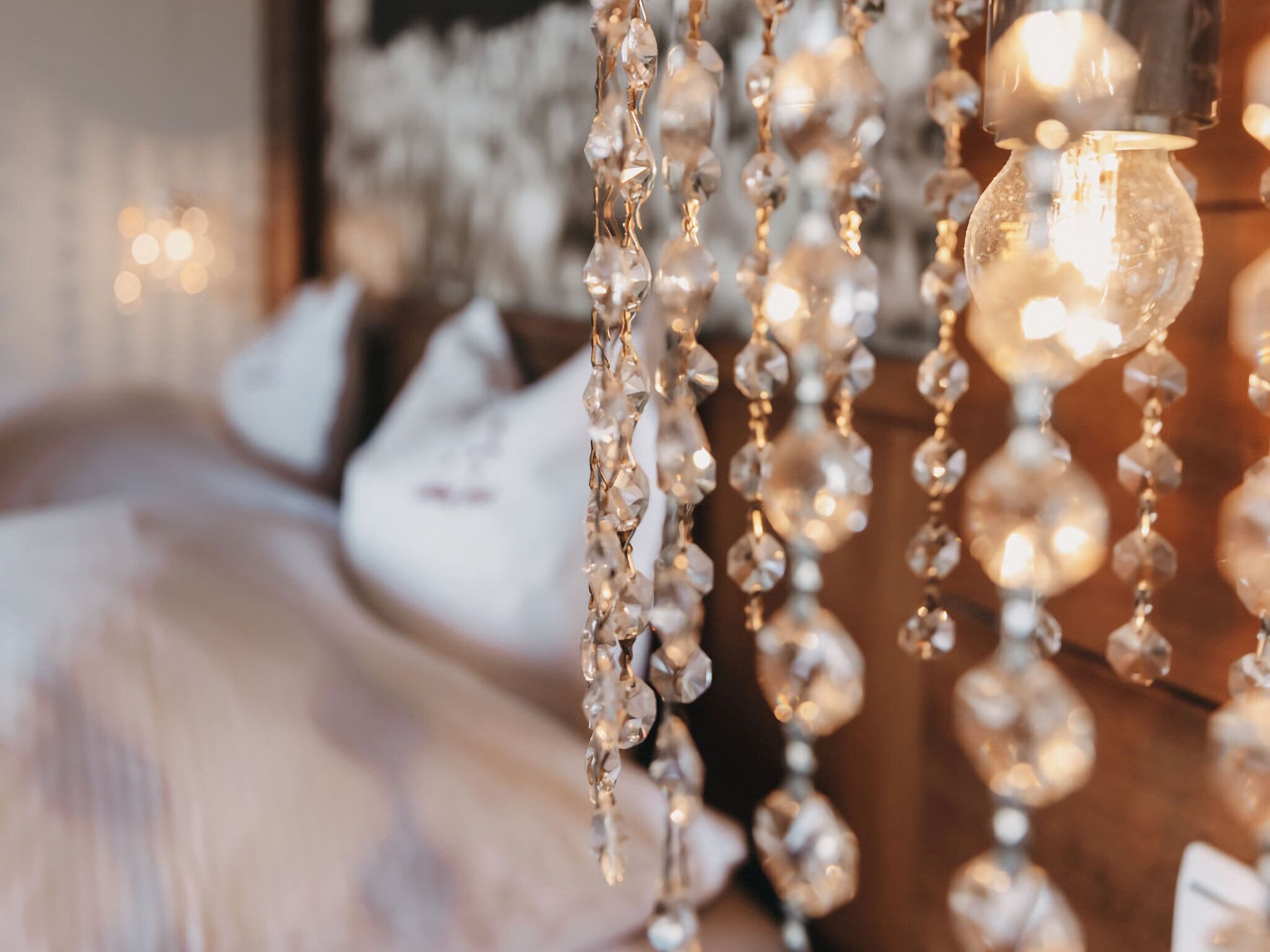 Una cama con ropa blanca, una lámpara de araña de cristal colgante y un aplique iluminado.