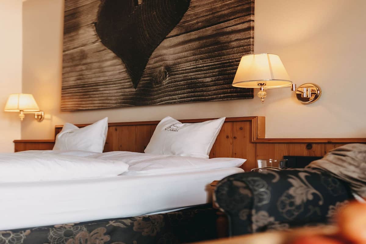Ein Hotelzimmer mit einem großen Bett, zwei Nachttischlampen, einem Wandbild eines Herzens und einem gemusterten Sessel.