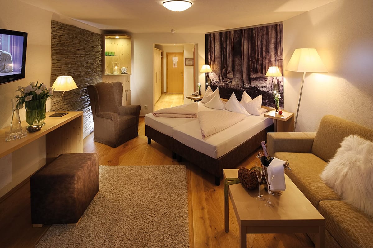 Ein Hotelzimmer mit Bett, Sofa, Schreibtisch, Stuhl, Fernseher und einem Bild an der Wand.