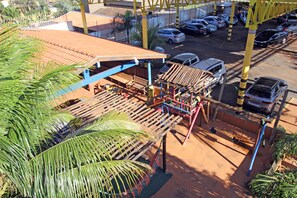 A parking area with multiple cars, a covered seating area with tables and chairs, and a palm tree in the foreground.