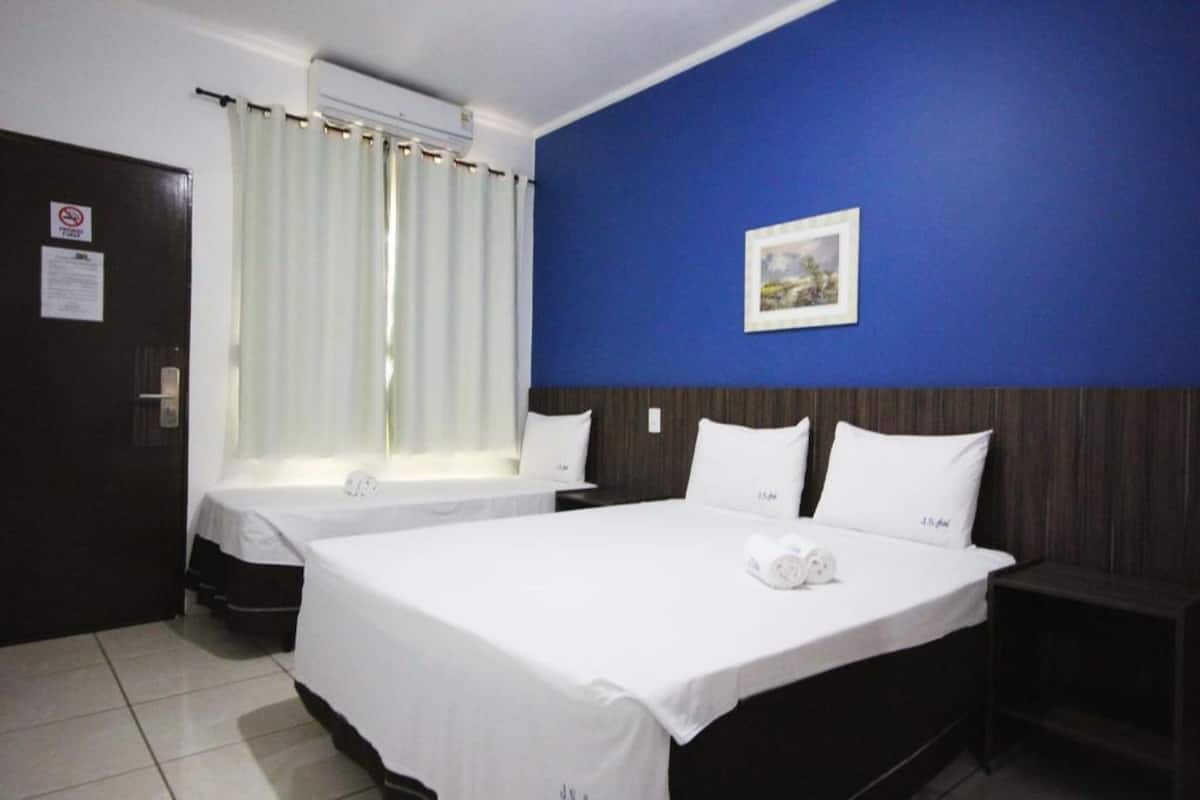 A hotel room with two beds, a blue accent wall, a framed picture, and a window with curtains.