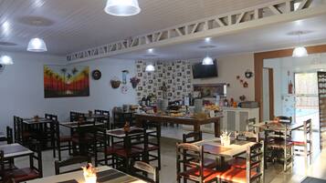 A restaurant with multiple tables and chairs, a kitchen area, and a television on the wall.