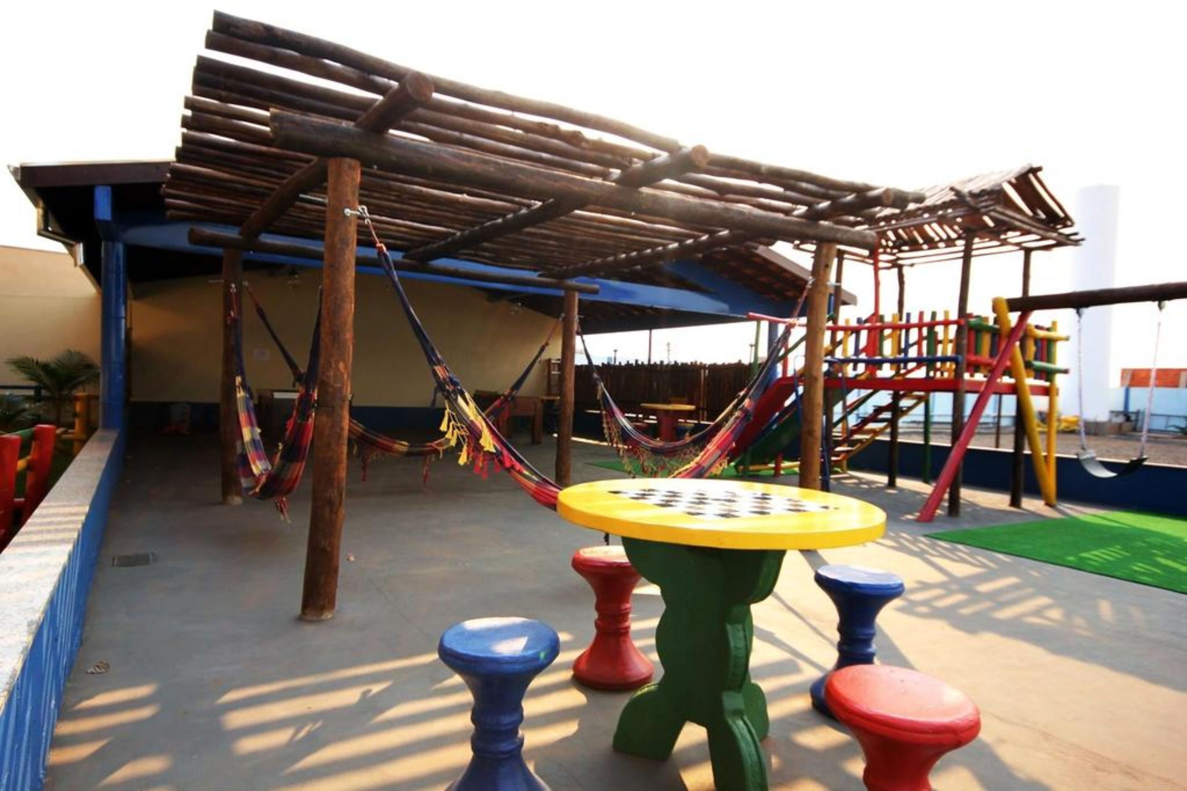 A playground with a wooden climbing structure, colorful play equipment, and a covered seating area.