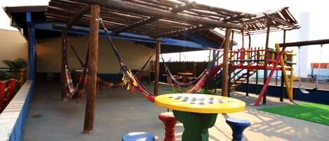 A playground with a wooden climbing structure, colorful play equipment, and a covered seating area.