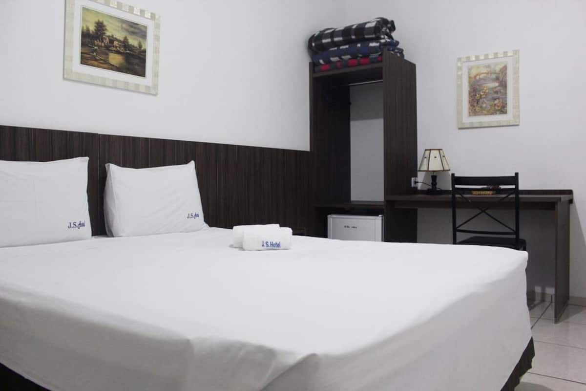 A hotel room with a bed, a desk, and a chair. There are two pillows with the hotel name on them.