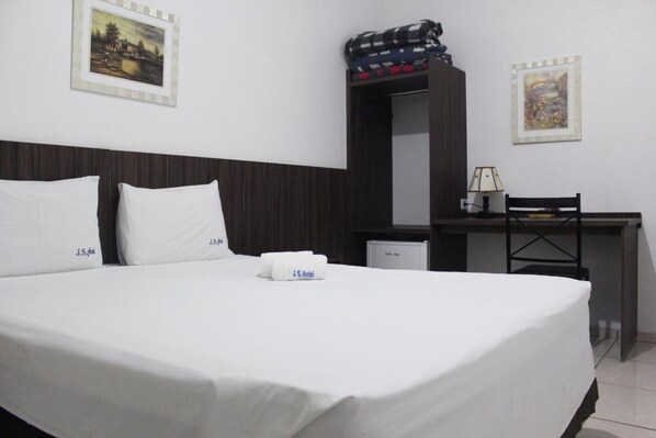 A hotel room with a bed, a desk, and a chair. There are two pillows with the hotel name on them.