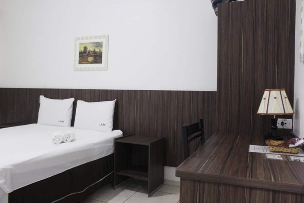 A hotel room with a bed, a small bedside table, a lamp, and a picture on the wall.
