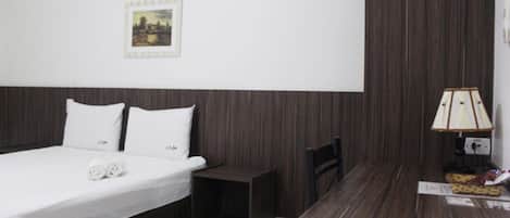 Una habitación de hotel con una cama, una mesita de noche pequeña, una lámpara y un cuadro en la pared.