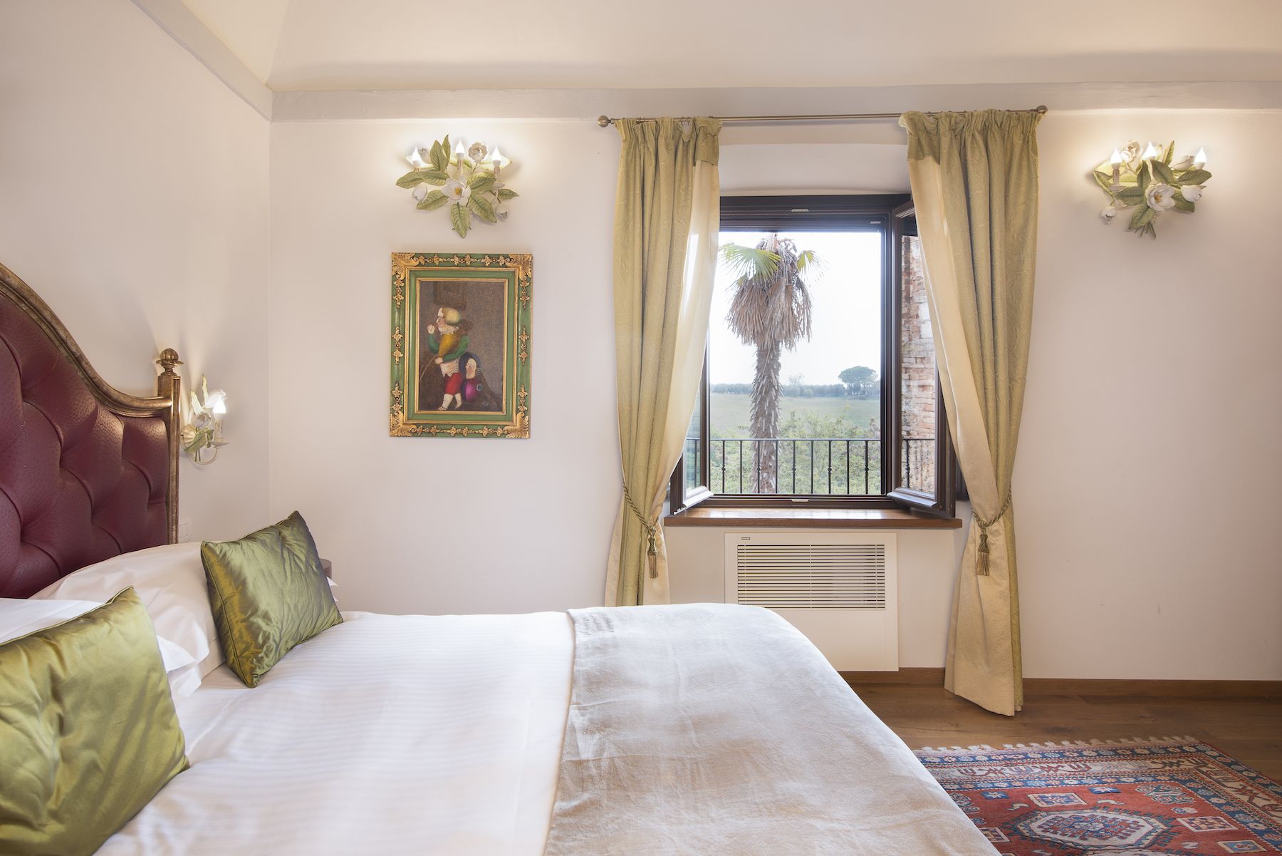 A bedroom with a large bed, a window with curtains, a framed picture on the wall, and a radiator.