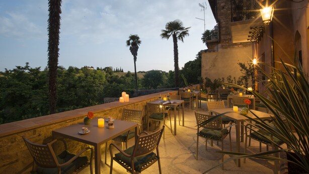 An outdoor dining area with tables and chairs, candles, and a view of palm trees and greenery. - Palazzo Pacini (Colle di Val d'Elsa)